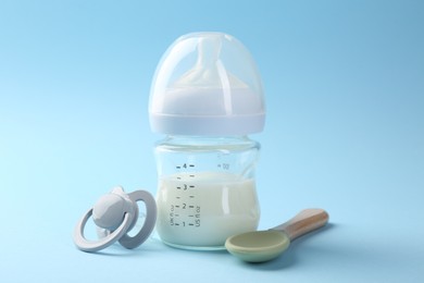 Feeding bottle with milk, spoon and pacifier on light blue background