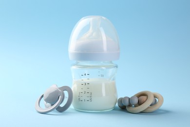 Feeding bottle with milk, teether and pacifier on light blue background