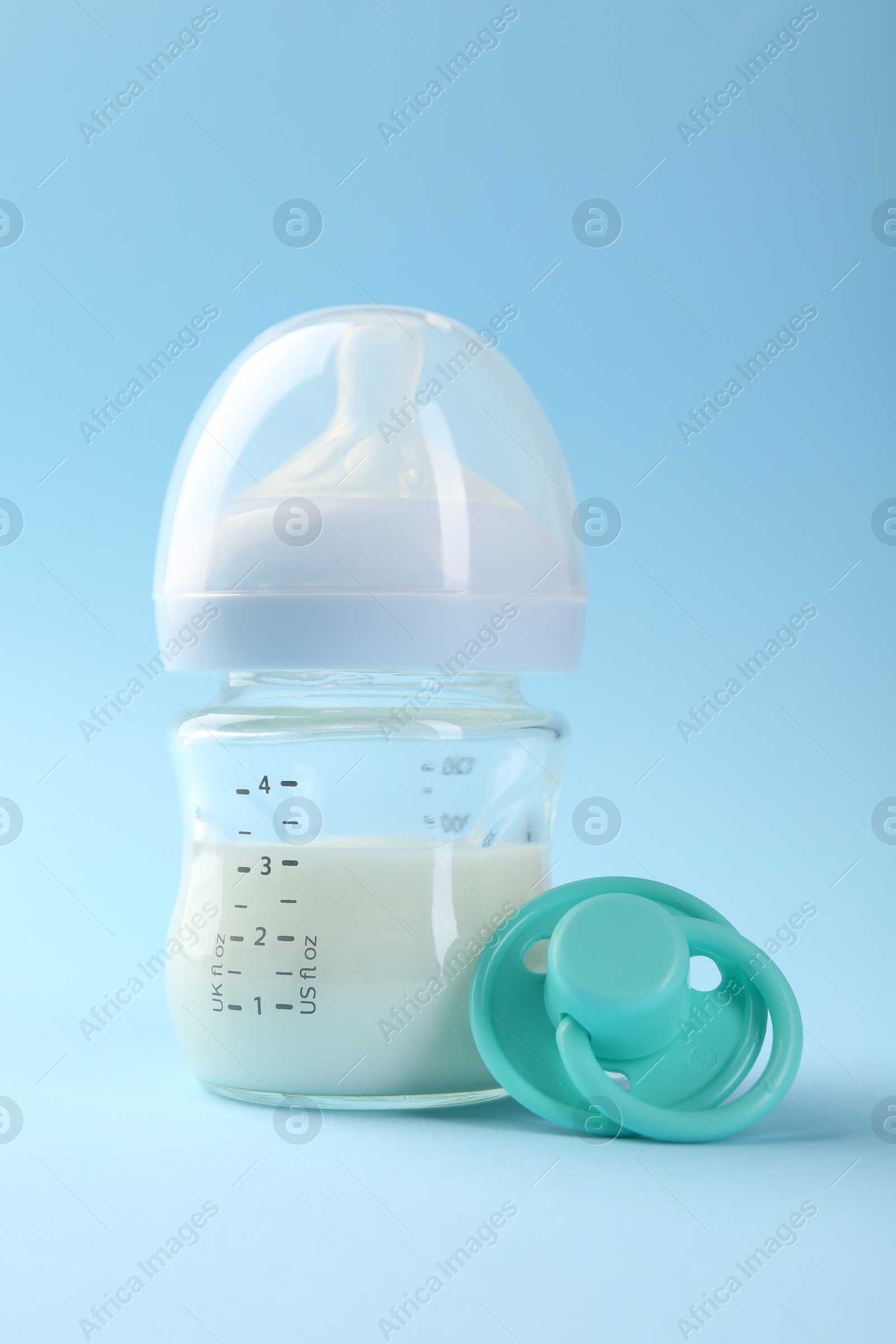 Photo of Feeding bottle with milk and pacifier on light blue background