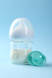 Feeding bottle with milk and pacifier on light blue background