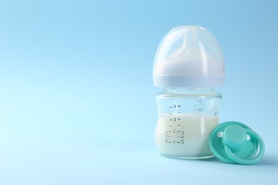 Photo of Feeding bottle with milk and pacifier on light blue background, space for text