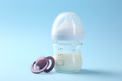 Feeding bottle with milk and pacifier on light blue background