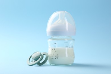 Feeding bottle with milk and pacifier on light blue background