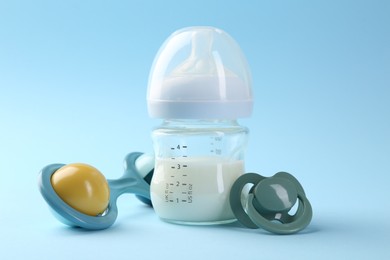 Feeding bottle with milk, pacifier and baby rattle on light blue background