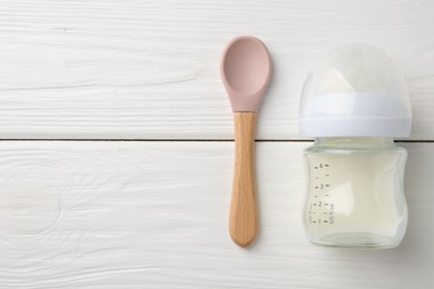 Feeding bottle with milk and spoon on white wooden table, flat lay. Space for text