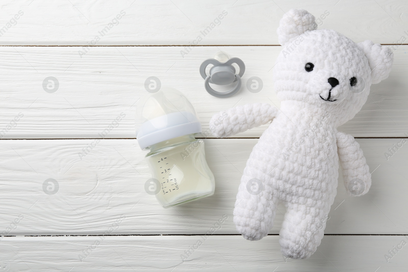 Photo of Feeding bottle with milk, toy bear and pacifier on white wooden table, flat lay. Space for text