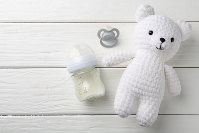 Photo of Feeding bottle with milk, toy bear and pacifier on white wooden table, flat lay. Space for text