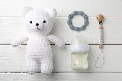 Photo of Feeding bottle with milk, toy bear and teethers on white wooden table, flat lay