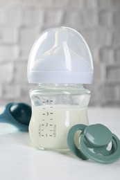 Feeding bottle with milk and pacifier on white table