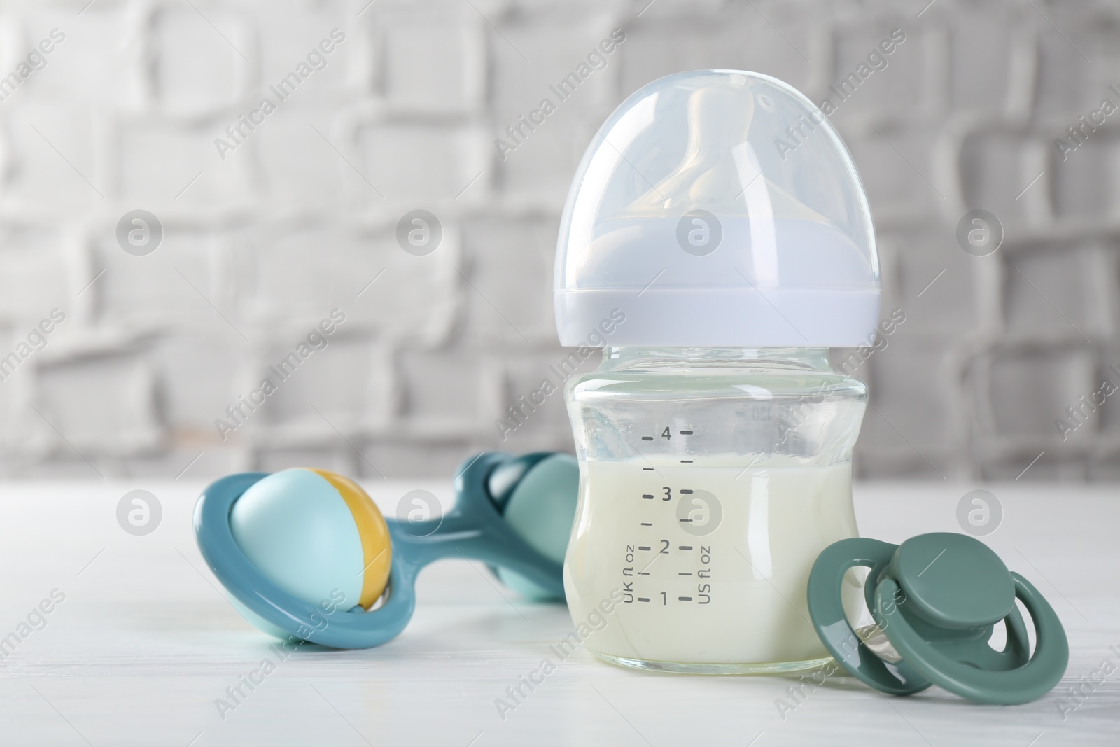 Photo of Feeding bottle with milk, baby rattle and pacifier on white wooden table