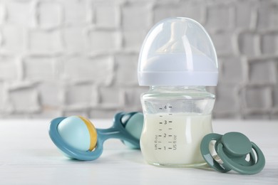 Feeding bottle with milk, baby rattle and pacifier on white wooden table