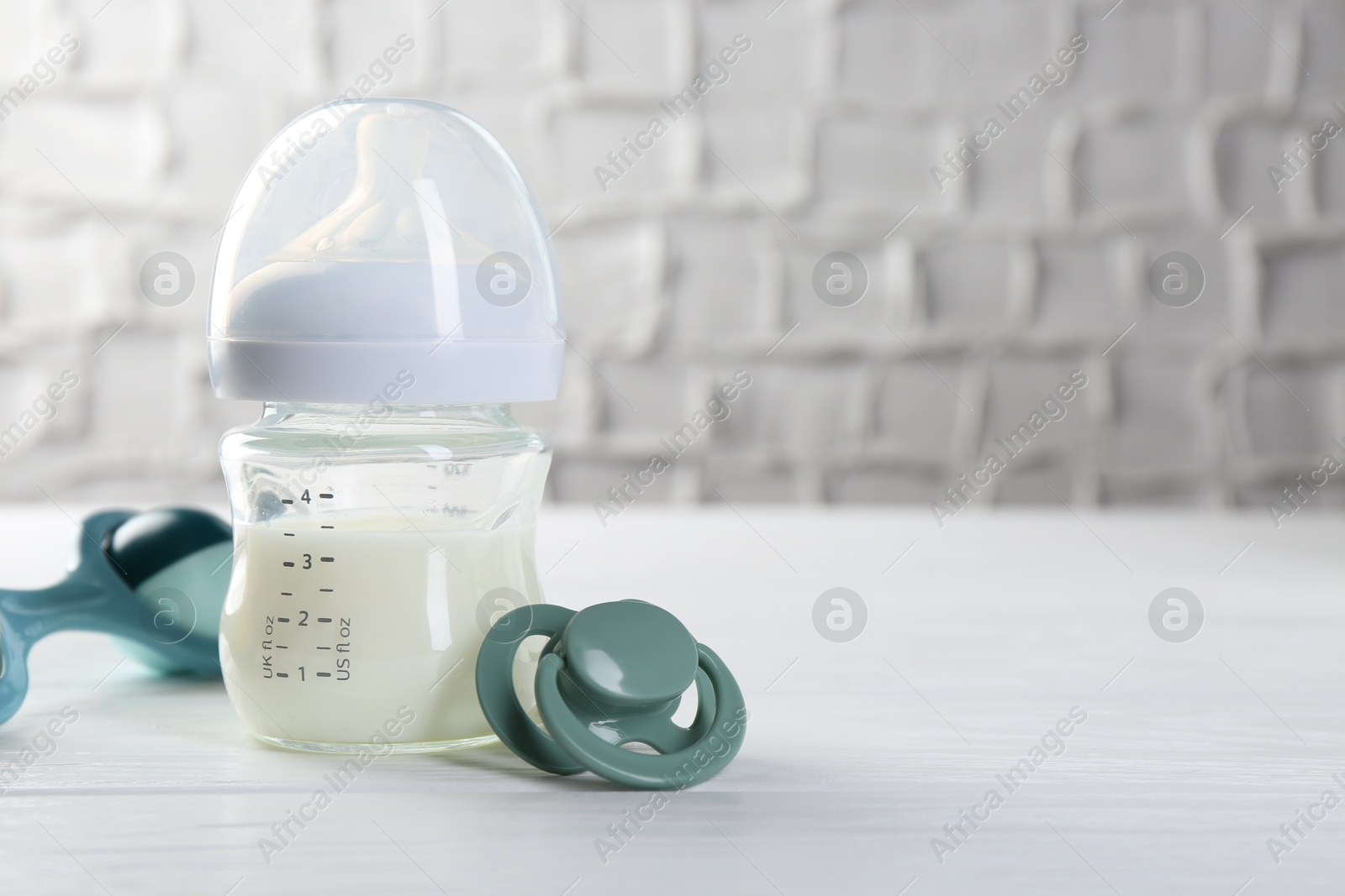 Photo of Feeding bottle with milk, pacifier and baby rattle on white wooden table, space for text