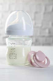 Photo of Feeding bottle with milk and pacifier on white wooden table