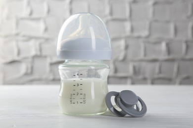 Photo of Feeding bottle with milk and pacifier on white wooden table