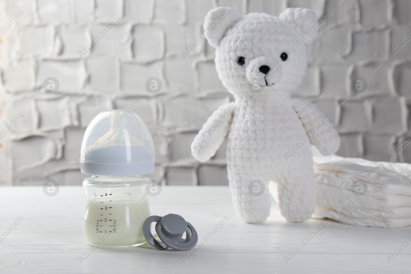 Photo of Feeding bottle with milk, pacifier, toy bear and diapers on white wooden table