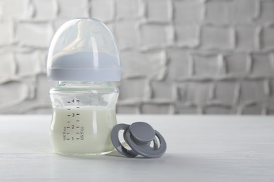 Feeding bottle with milk and pacifier on white wooden table, space for text