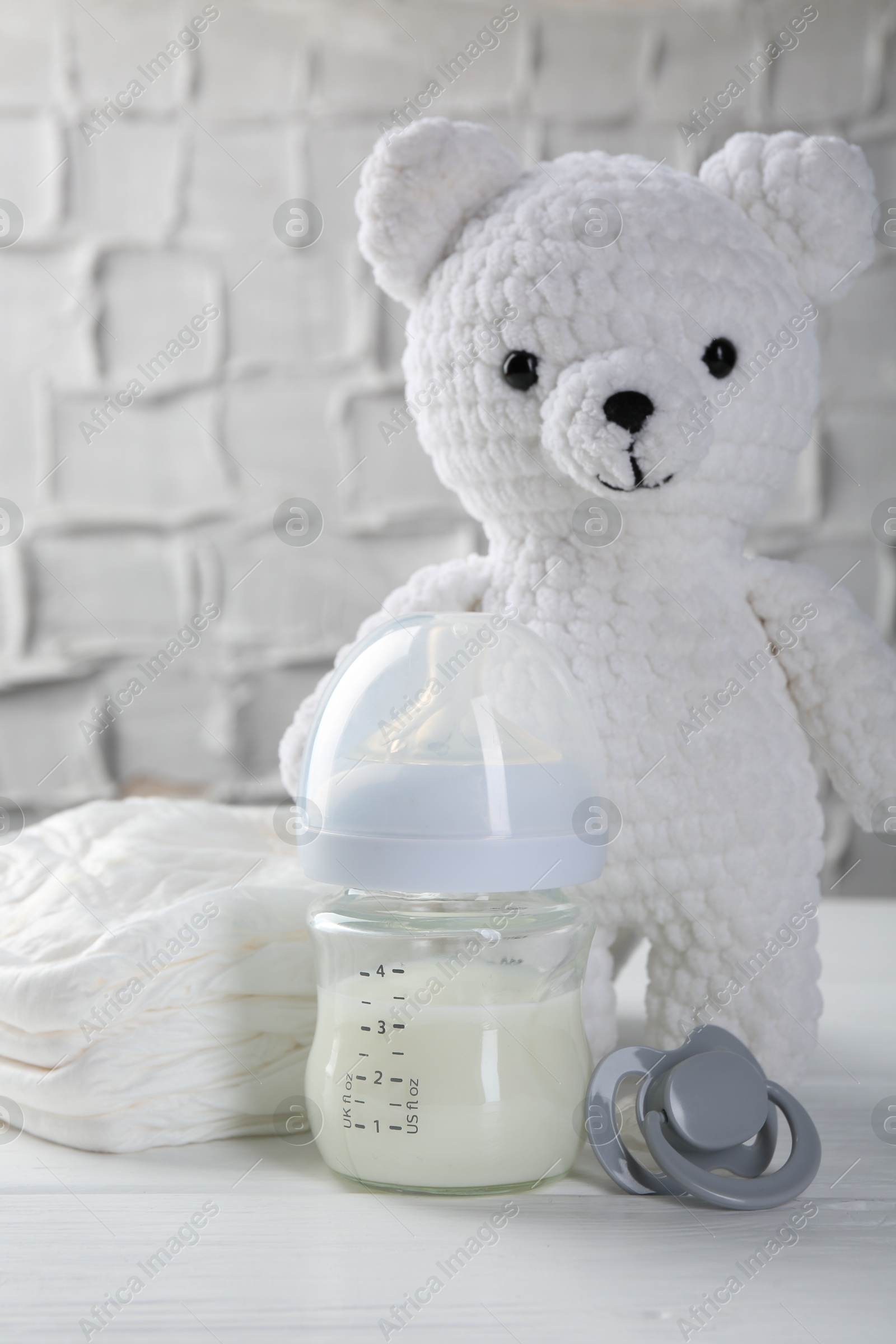 Photo of Feeding bottle with milk, toy bear, diapers and pacifier on white wooden table