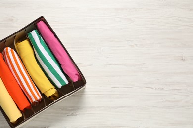 Photo of Organizer with folded clothes on wooden table, top view. Space for text