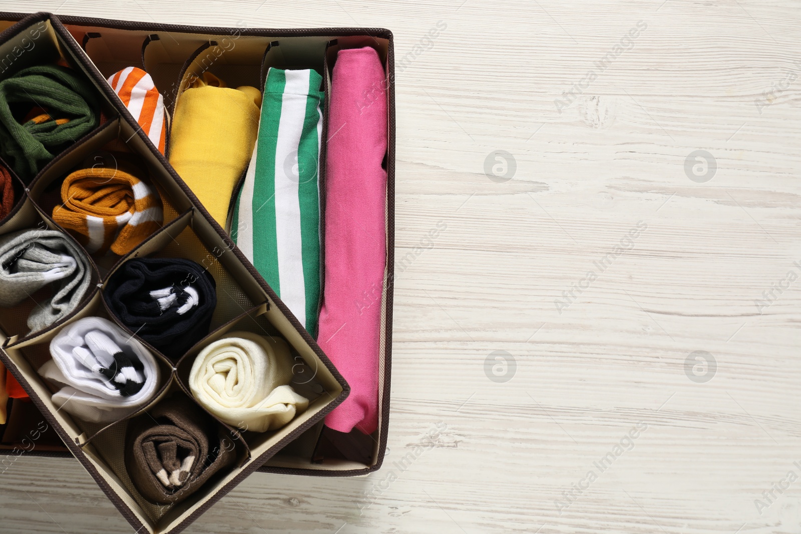 Photo of Organizers with folded clothes on wooden table, top view. Space for text