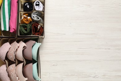 Organizers with folded clothes and underwear on wooden table, flat lay. Space for text