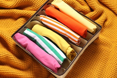 Organizer with folded clothes on orange blanket, above view