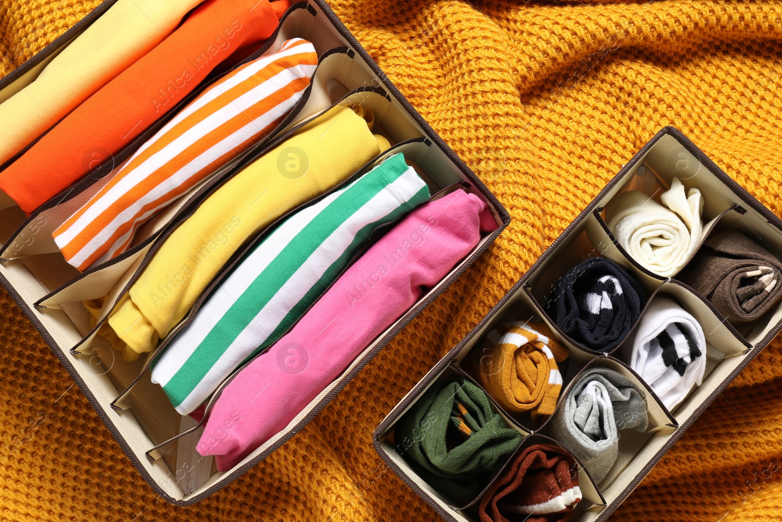 Photo of Organizers with folded clothes on orange blanket, flat lay