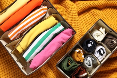 Organizers with folded clothes on orange blanket, flat lay