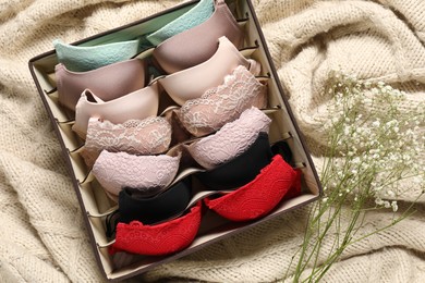 Organizer with bras and flowers on beige blanket, flat lay