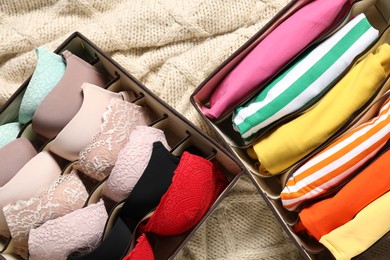 Organizers with folded clothes and underwear on beige blanket, flat lay