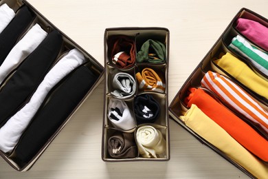 Organizers with folded clothes on light wooden table, flat lay