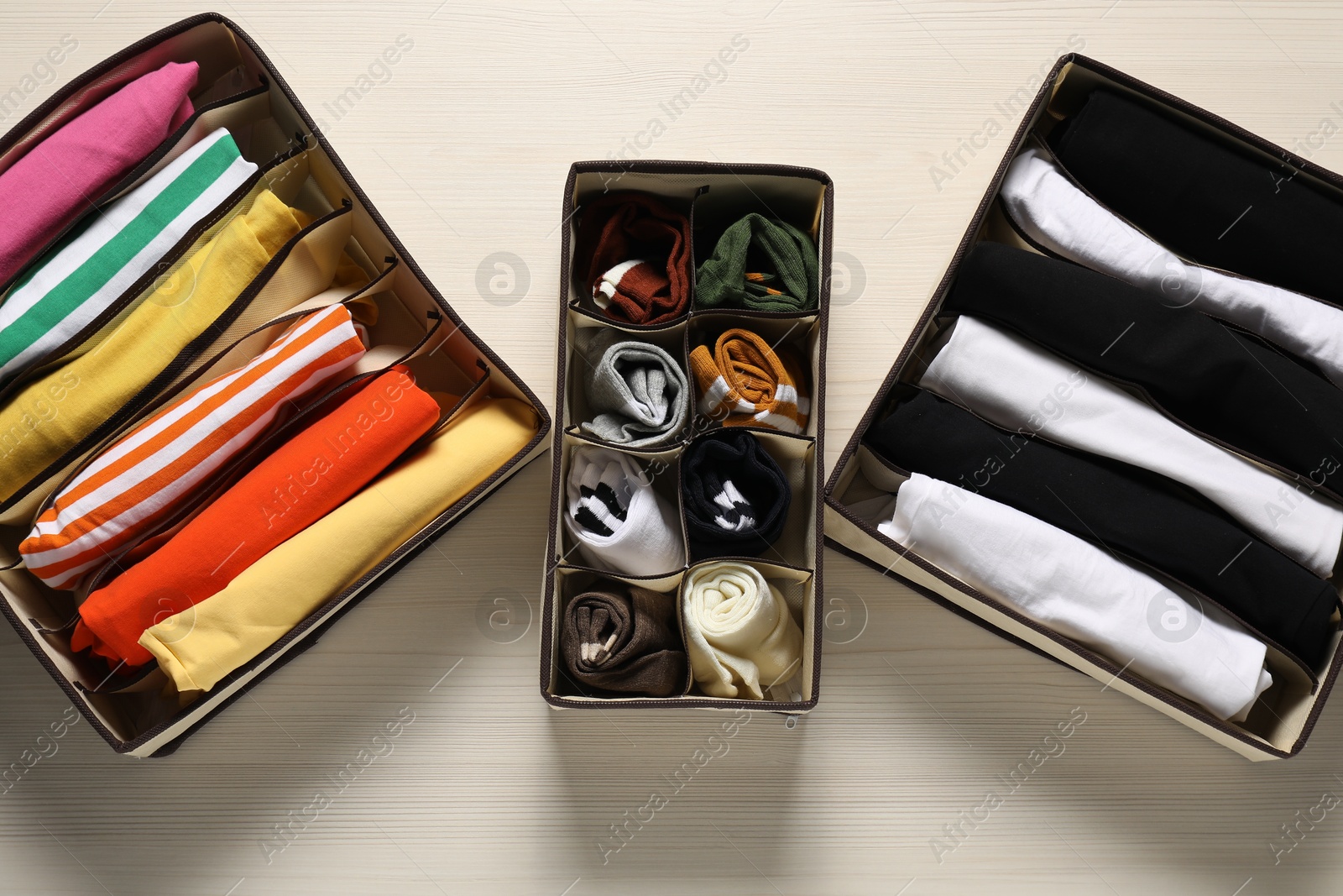 Photo of Organizers with folded clothes on light wooden table, flat lay