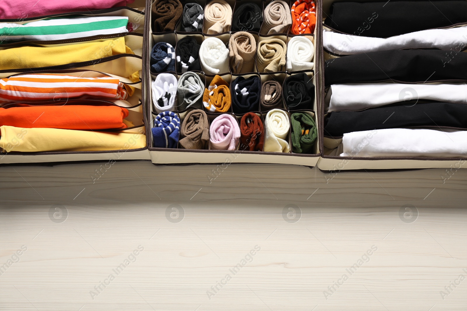 Photo of Organizers with folded clothes on light wooden table, flat lay. Space for text