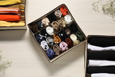 Organizers with folded clothes and flowers on light wooden table, flat lay