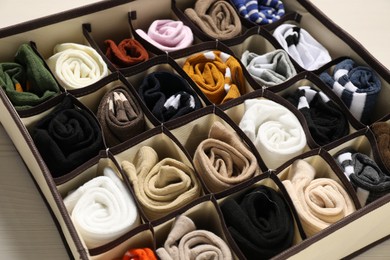 Photo of Organizer with different socks on light wooden table, closeup