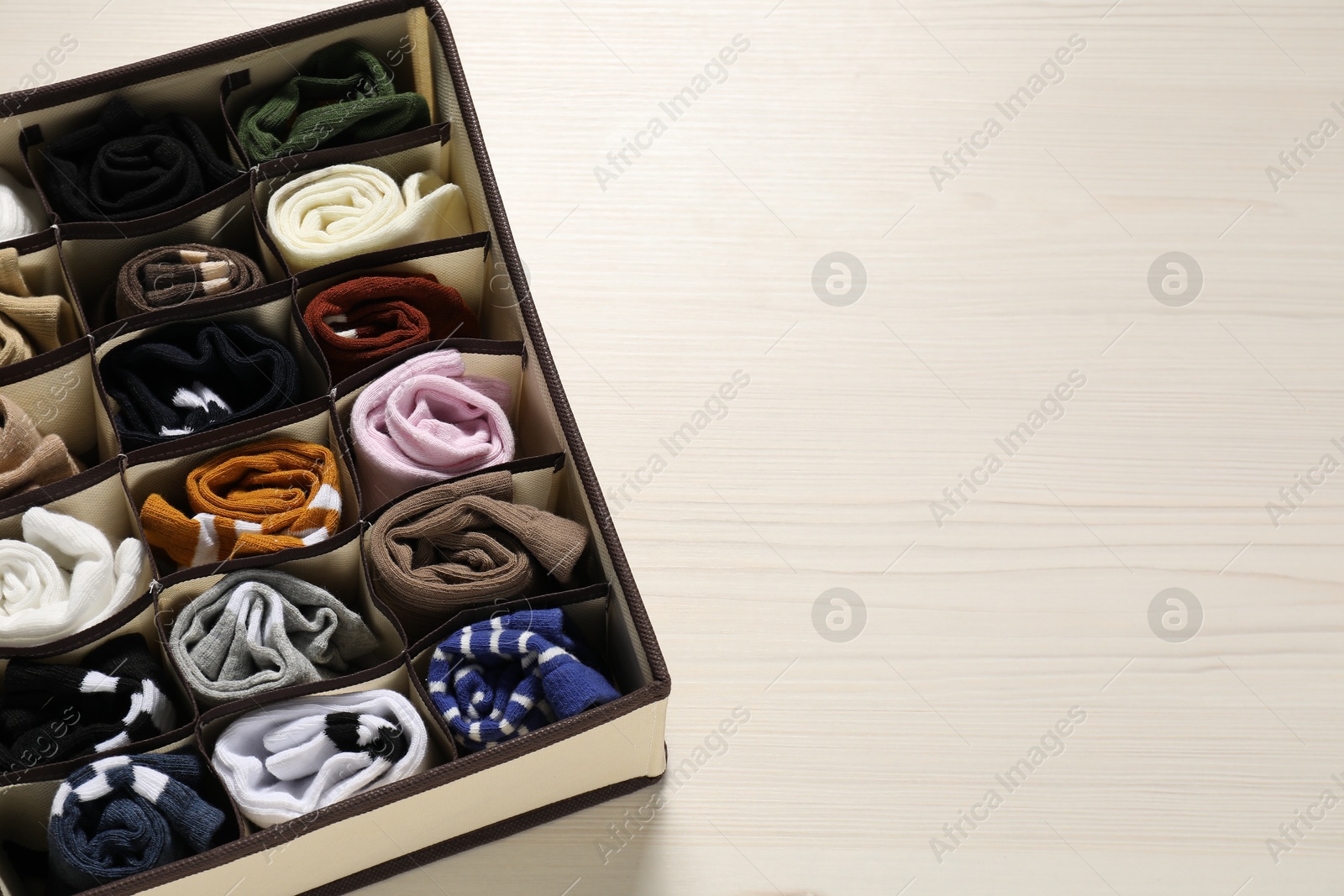 Photo of Organizer with different socks on light wooden table, above view. Space for text