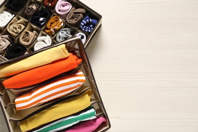 Photo of Organizers with folded clothes on light wooden table, top view. Space for text