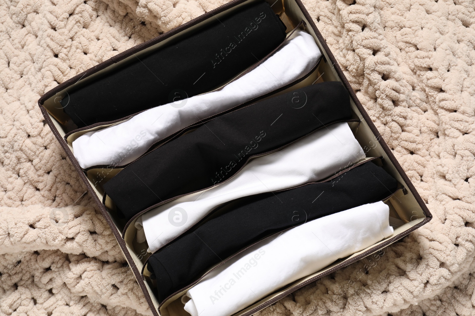 Photo of Organizer with folded clothes on beige blanket, top view