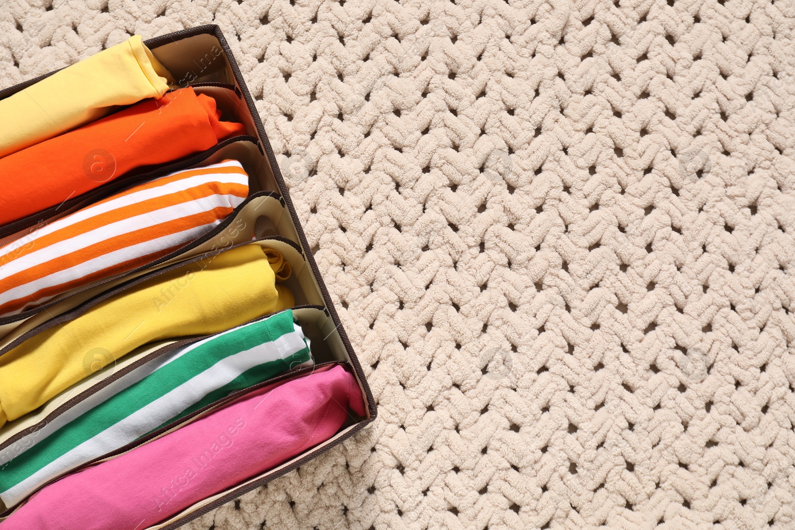 Photo of Organizer with folded clothes on beige blanket, top view. Space for text