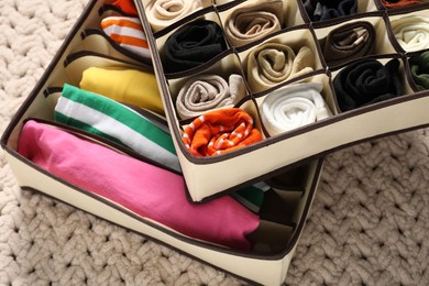 Photo of Organizers with folded clothes on beige blanket, above view