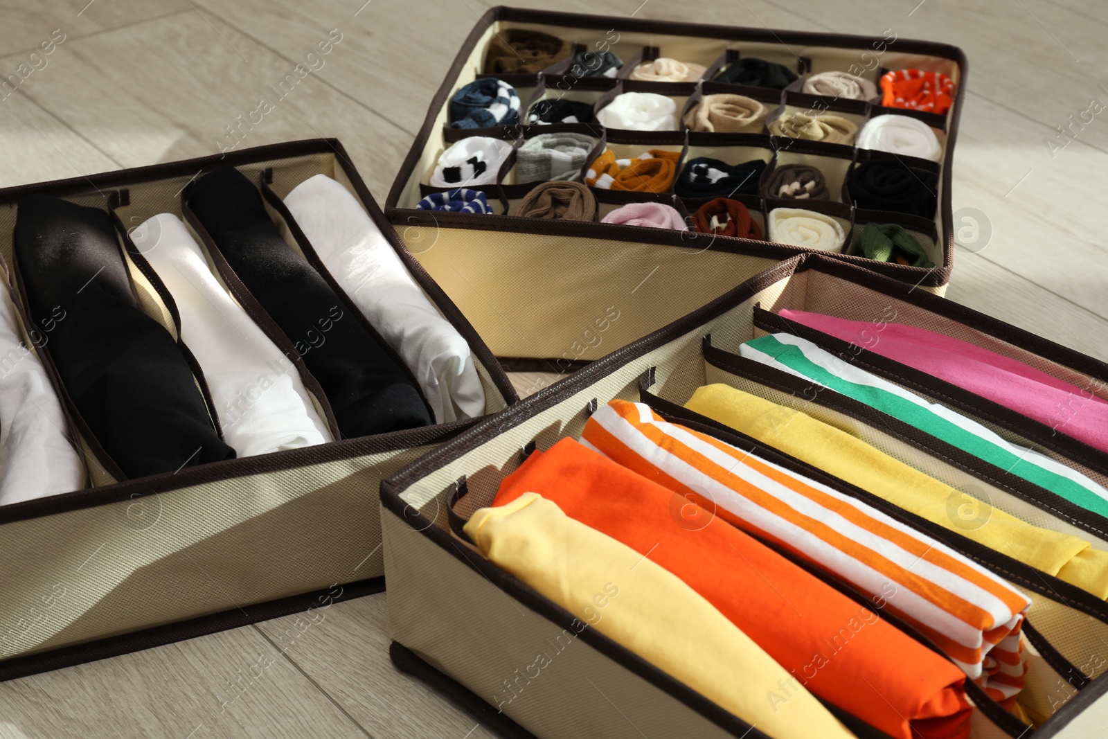 Photo of Organizers with folded clothes on wooden floor, closeup