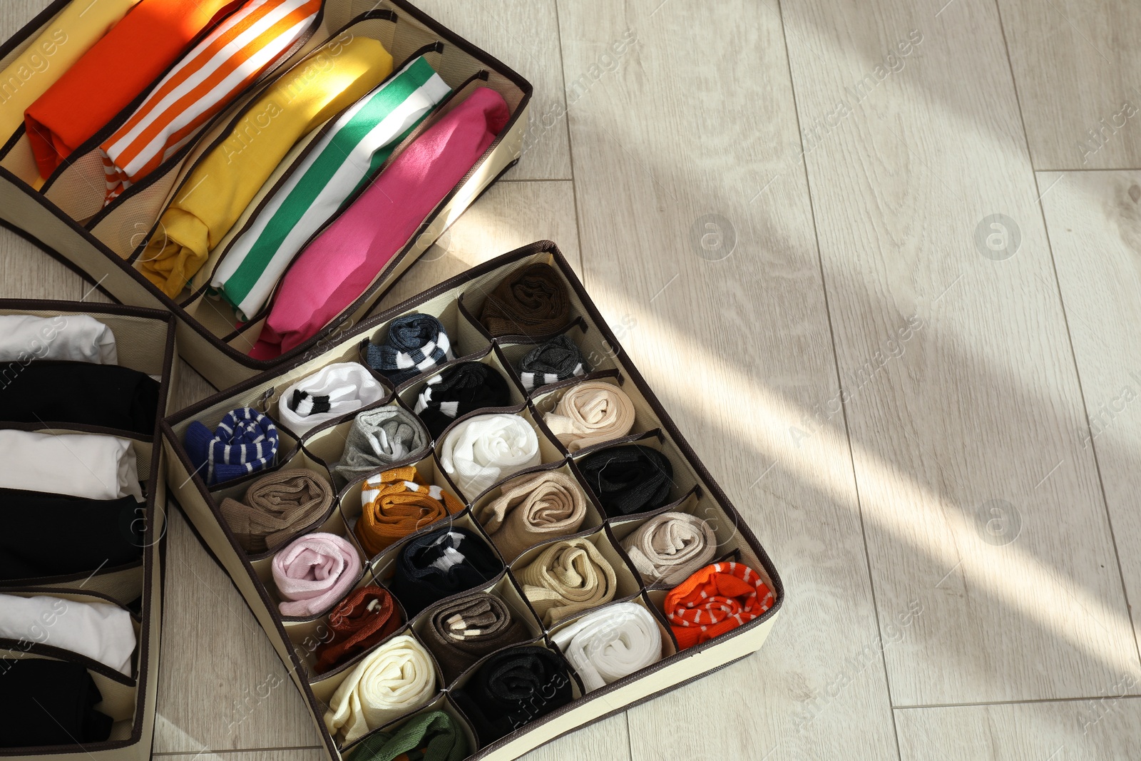 Photo of Organizers with folded clothes on wooden floor, above view. Space for text