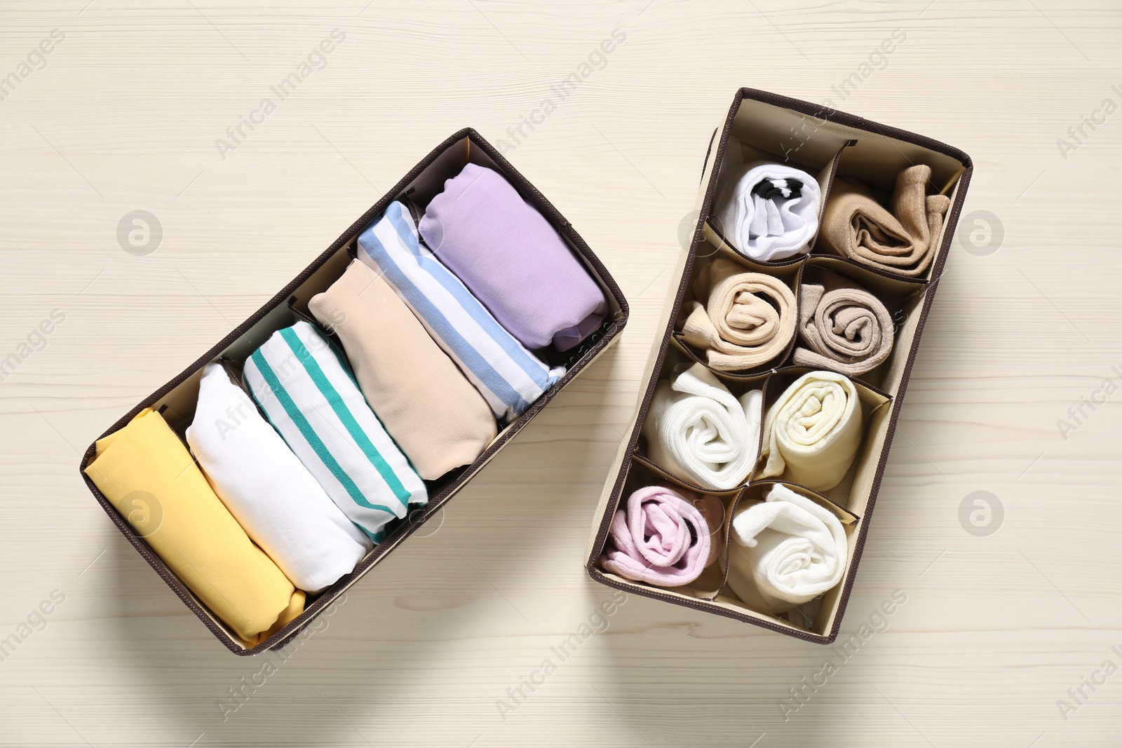 Photo of Organizers with folded clothes on light wooden table, flat lay