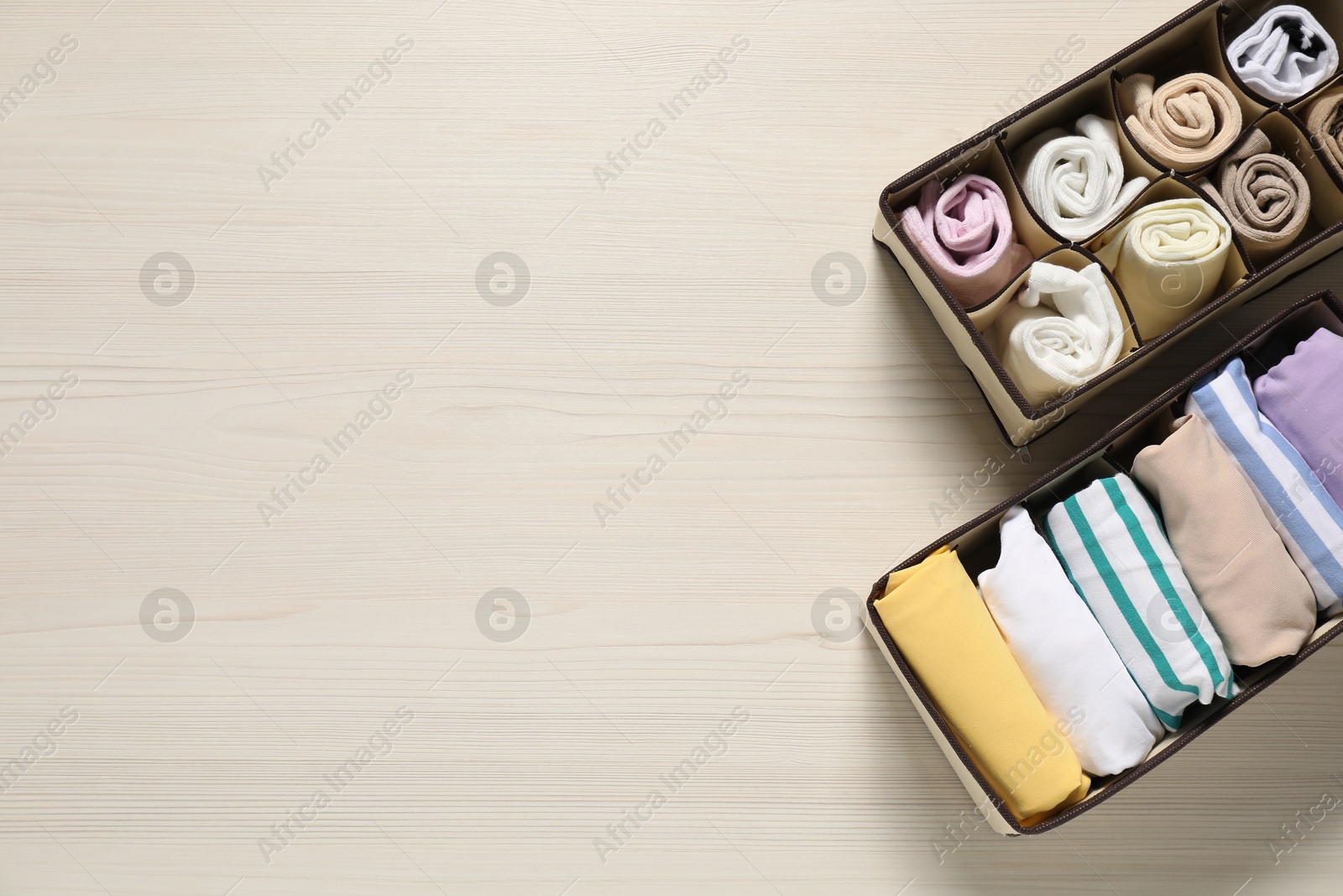 Photo of Organizers with folded clothes on light wooden table, flat lay. Space for text