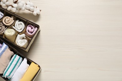 Organizers with folded clothes and cotton branch on light wooden table, flat lay. Space for text