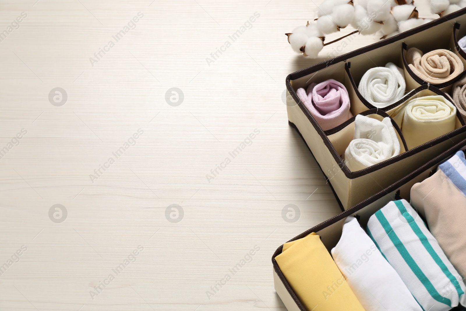 Photo of Organizers with folded clothes and cotton branch on light wooden table, above view. Space for text