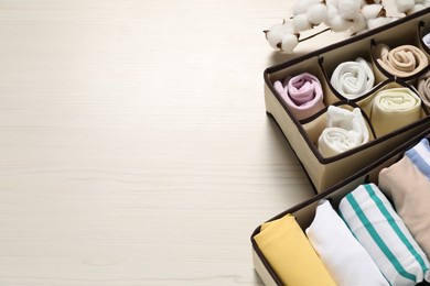 Photo of Organizers with folded clothes and cotton branch on light wooden table, above view. Space for text