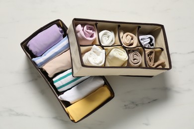 Organizers with folded clothes on white marble table, top view