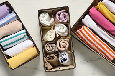 Organizers with folded clothes on white marble table, flat lay