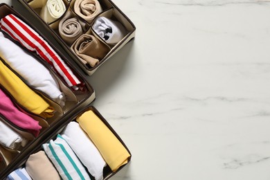 Photo of Organizers with folded clothes on white marble table, flat lay. Space for text