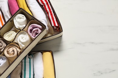 Photo of Organizers with folded clothes on white marble table, flat lay. Space for text